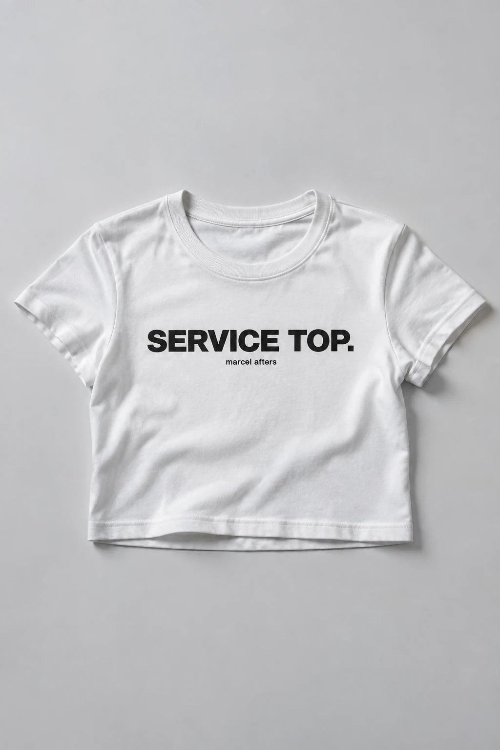 White Service Top shirt concept, laid flat with its black slogan and Marcel Afters signature fully visible.